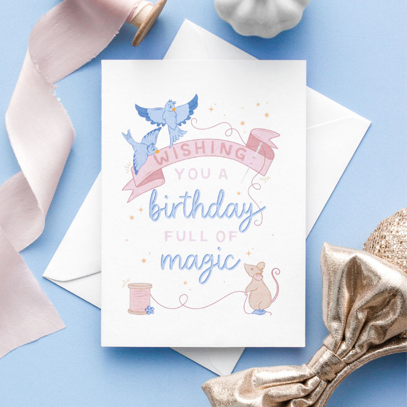 A birthday card with a hand drawn image of a mouse with a cotton reel and sewing needle, two blue birds holding pink ribbon. Could easily be the dress making scene from Cinderella. The card caption is: Wishing You A Birthday Full Of Magic